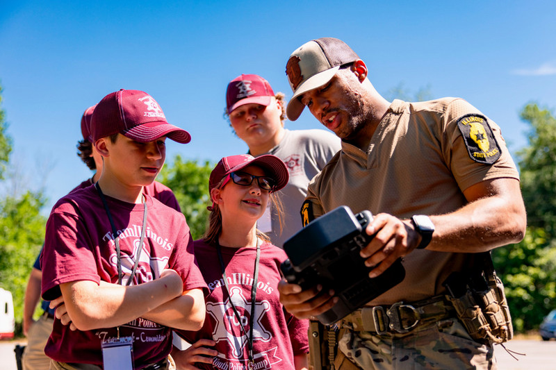 A Illinois State Police officer shows three teenagers a display connected to a drone. 