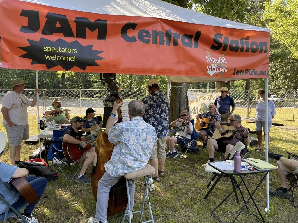 several people playing string intruments gathered and participating in music lessons under the Jam Central Station tent 